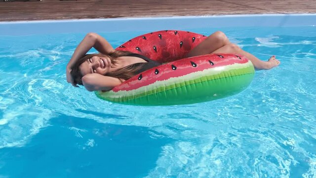 Beautiful woman in swimming pool close view from side, young girl in bikini relaxes and swims on inflatable ring watermelon and has fun in water on family vacation, tropical holiday resort