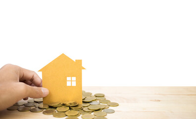 Hand holding house paper cut and stack of cions on wooden table with white background, investment...
