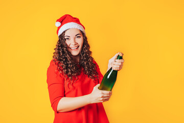 Young woman in red dress and christmas hat opens a bottle