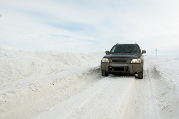 Male driver in a black dirty car on a winter road cleared of snow, drifts along the road