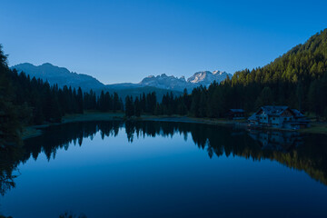 Early morning in the Alps. House in the mountains by a mountain lake. Reflections of trees, mountains, sky in a mountain lake.