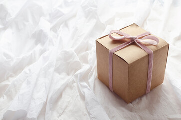 Cute little present box with pink ribbon and bow on it, white wrapping paper.Empty space