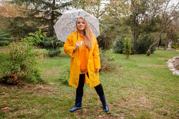 Caucasian girl in a yellow raincoat walking outside in the rainy day in autumn. People in fall concept. Yellow rain coat concept.