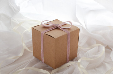 Closeup of craft paper gift box with pink ribbon and bow on the white tissue paper