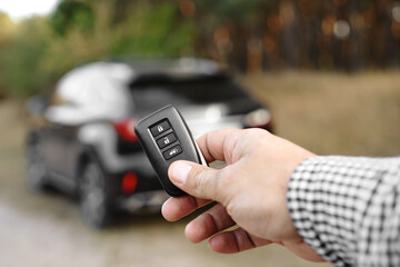 Man hand holds car key against blurred car. New car concept.
