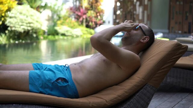 Man relaxing, taking nap on sunbed by swimming pool