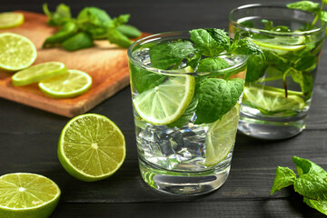 Two glasses of lemonade or mojito cocktail with ice, fresh mint and lime. Cold refreshing cocktail on black table.