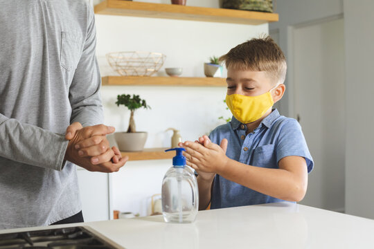 Boy wearing face mask sanitizing his hands at home