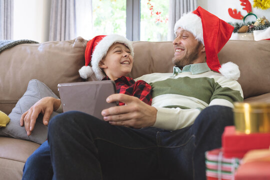 Man and son wearing Santa hat using digital tablet at home