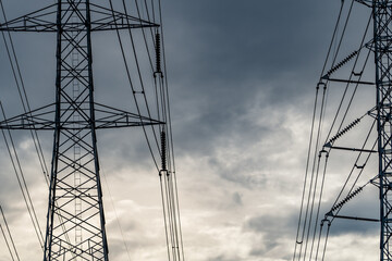 High voltage electric pylon and electrical wire against stormy sky and clouds. Bottom view of electric pylon. High voltage grid tower with wire cable. Transmission lines on high voltage grid tower.