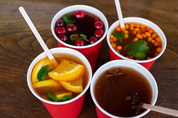 Winter sweet warming alcoholic, non-alcoholic drinks on wooden table. Mulled wine with honey, sea buckthorn, cherries, cranberries, star anise, mint, cinnamon. Winter entertainment, leisure, fairs
