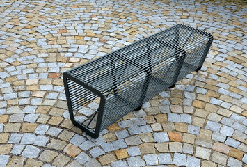 bench without backrest made of metal rods. lattice transparent placed on gypsum cobblestone paving...