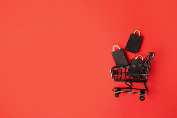 black paper bags in shopping cart on red background, copy space. black friday concept