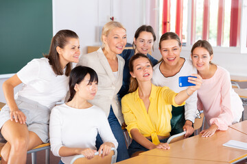Fototapeta na wymiar Cheerful female students with woman teacher making selfie in auditorium