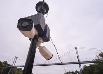 Security camera hanging among wire in guarded bridge with cloudy sky background.