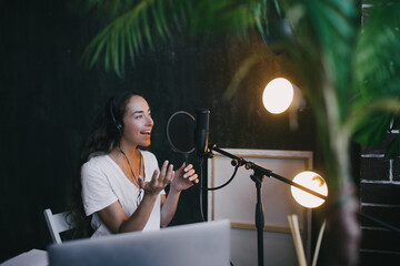 Woman blogger with long black hair recording online podcast using her laptop, headphones and...