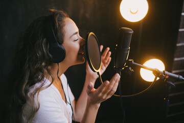 Young beautiful woman singing in microphone, recording voice in a studio.