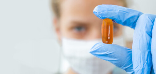 The doctor holds a pill of omega vitamins in his hand - obrazy, fototapety, plakaty