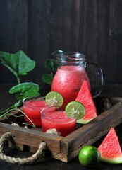 Jus Semangka or Watermelon juice garnished with lime slice on rustic wooden tray. Dark wooden...