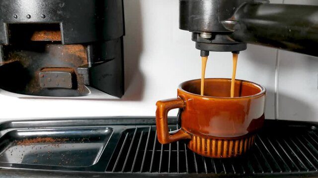 Close Up Of Coffee Machine Pours Coffee Into A Brown Cup. Coffee Spills Over The Edge Of The Cup (overflow)