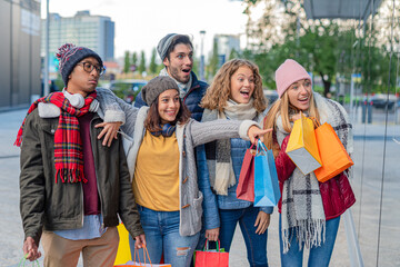 multi-ethnic group of friends around the city shopping, the brunette girl stops the company to show...