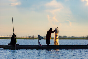 Silhouette of asian Fisherman on a traditional wooden boat during sunrise.