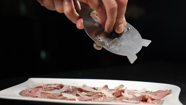 Traditional French or Italian cuisine, gourmet cuisine, truffles, fine dishes. Chef grating rare black truffle on slices of roast beef. Slow motion. Luxury restaurant. Full hd