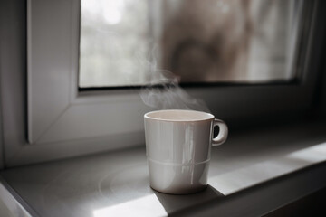 Cup of coffee with steam on windowsill by the window.