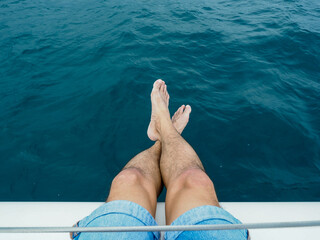 Closeup of a man legs sitting on a crusing yacht.