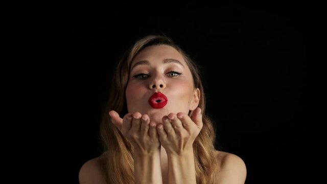 Young optimistic beautiful woman with red lipstick posing isolated over black background and blowing kisses
