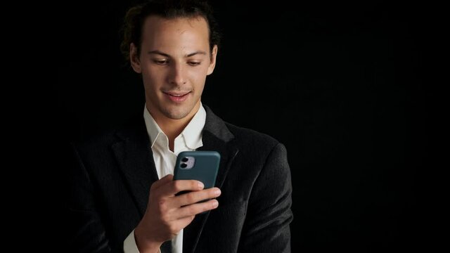 Young handsome concentrated man in a suit using mobile phone isolated over black background