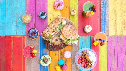 Colorful and tasty drinks and snaks with smoothies, cupcakes, donuts and sandwiches on a colorful wood table