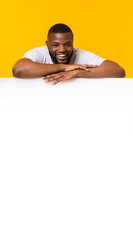 Happy black man leaning on white empty board for advertisement