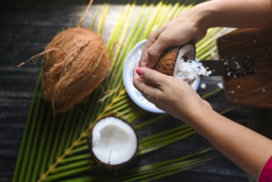 Woman sit on coconut grater to grate coconut into bowl palm leaf background Kerala India. Make grated coconut, coconut flakes make coconut milk Home by squeezing for cooking curry, virgin coconut oil.
