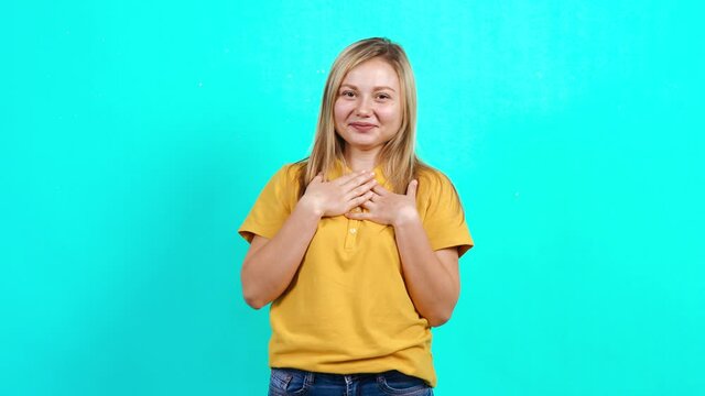 The excited young woman points to the room and smiles broadly. Beautiful Caucasian woman in yellow T-shirt and long blond hair standing on blue background. A little fat teenager. Advertising concept.