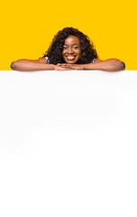 Smiling black woman leaning on white empty board for advertisement