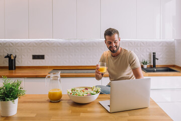 Smiling young man using laptop studying working online at home