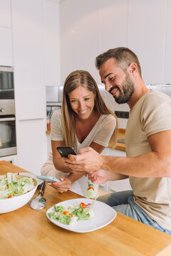 Lovely couple having breakfast and looking photos in mobile phone in the kitchen at home