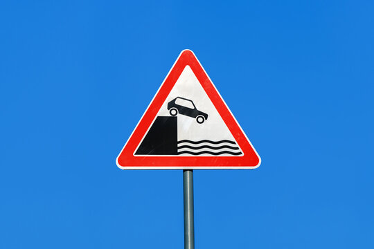 International road sign 'Unprotected quayside or riverbank'. It's showing car falling into the water