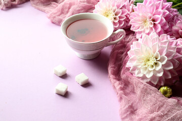 Bouquet of delicate dahlias with a Cup of tea and pieces of white sugar on a pastel background, close - up, space for text