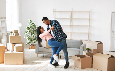 Loving black couple dancing in their house among carton boxes on moving day