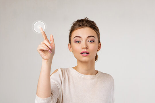 young beautiful woman pressing virtual button and looking at the camera on gray background.