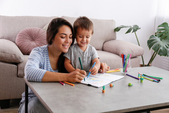 Young Beautiful Woman Teaching Her Two Year Old Son To Draw At Home. Woman Spending Quality Time With Her Toddler Child. Close Up, Copy Space, Background.