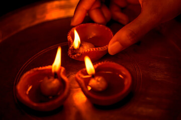 Indian woman or girl holding a lit clay diya in her hand and illuminating other oil lamps with it...