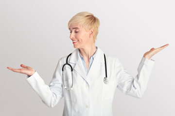 Adult woman doctor in white coat with stethoscope raises her hands for weighing