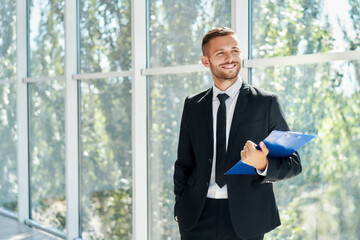 Handsome smiling businessman with clipboard in a bright modern office