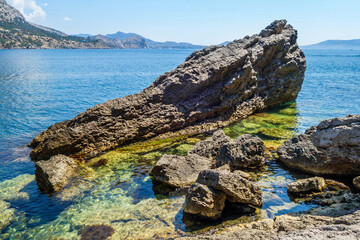 Huge coastal stones nearby shoreline of sea. Sunlight playing in calm waters. Shot in Black Sea resort Noviy Svit, Crimea