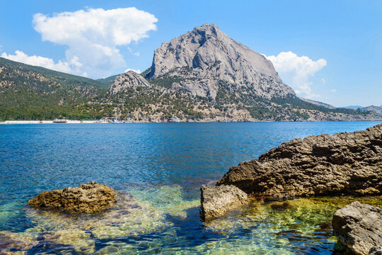 Panorama of Green Bay in resort town Noviy Svit, Crimea. Coastal stones & underwater reefs are on foreground, mountain Sokol (Falcon) & forest are on background