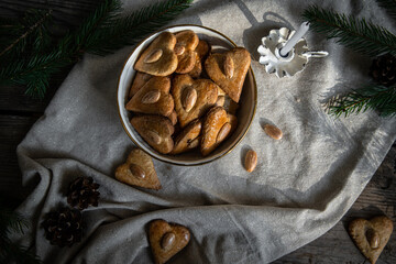 Bowl with heart-shaped gingerbread cookies with almond, espresso coffee, candle and fir branches on linen glittering fabric on wooden background,