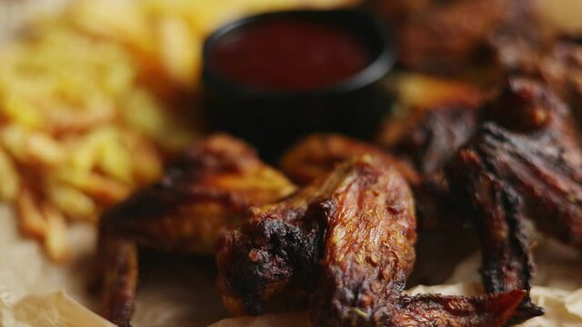 Appetizing roasted chicken wings and french fries with barbecue dip, served on baking paper
